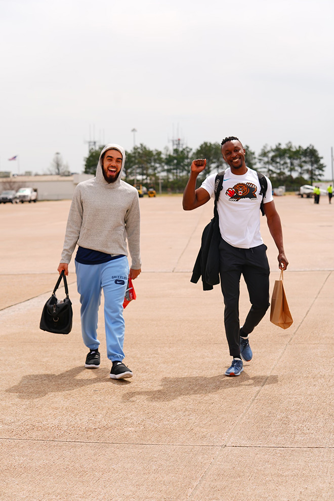 Jarred Boyd and another man walk across an airport tarmac carrying small bags
